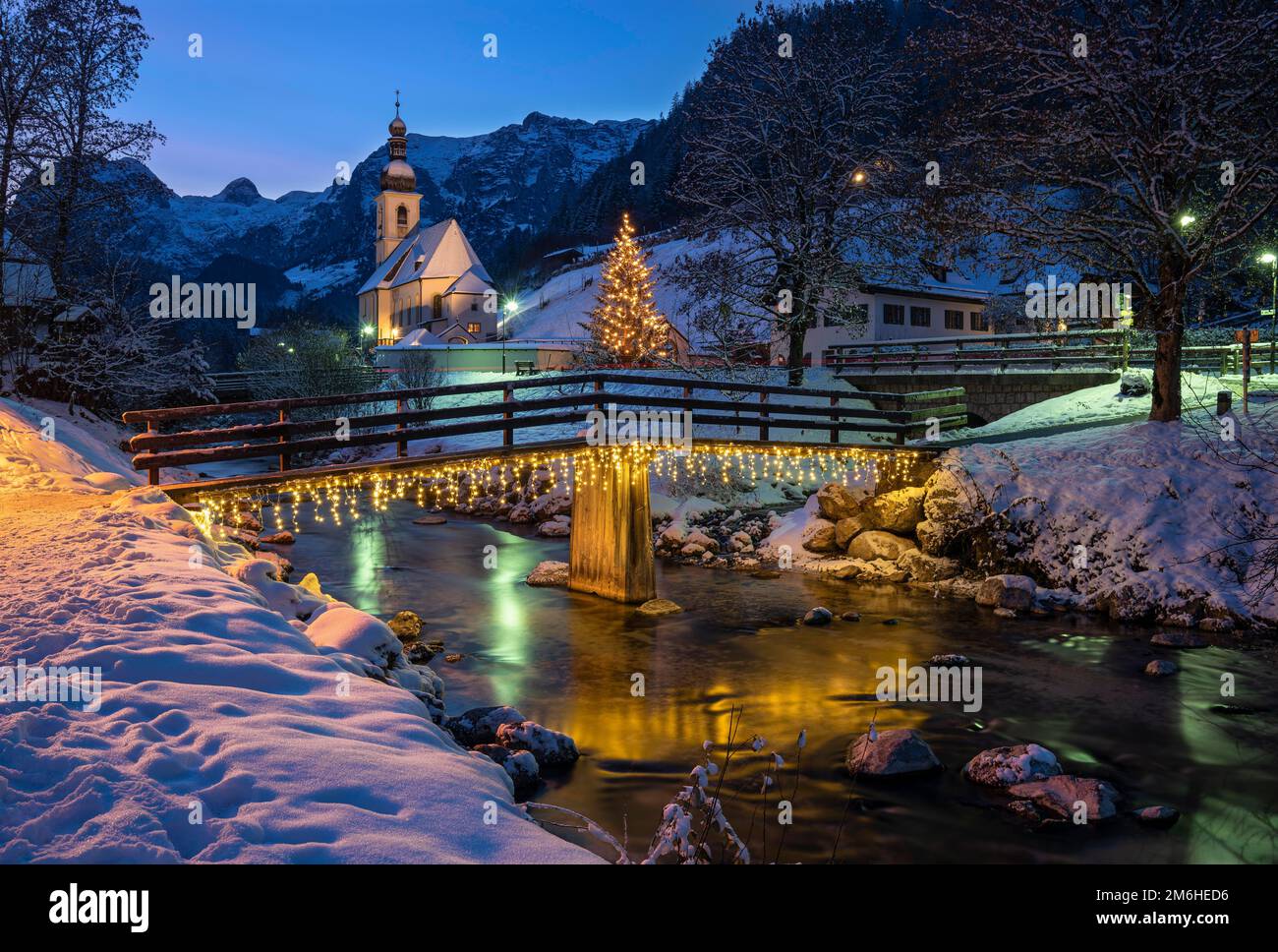 Église paroissiale de Winterly Sebastian à l'heure bleue, avec un pont en bois illuminé de noël au-dessus d'un ruisseau, longue exposition, Ramsau, Berchtesgadener Banque D'Images