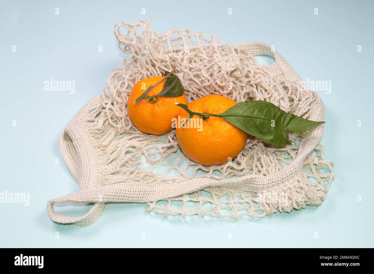 Mandarines mûres dans un sac à ficelle sur fond bleu. Fruits dans un emballage écologique Banque D'Images