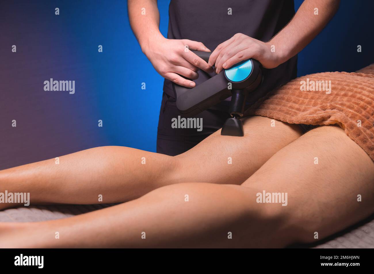 Masseuse masculine effectuant des exercices de massage sur les cuisses avec l'aide d'un masseur à percussion vibrato à un client masculin. Thérapie de choc Banque D'Images