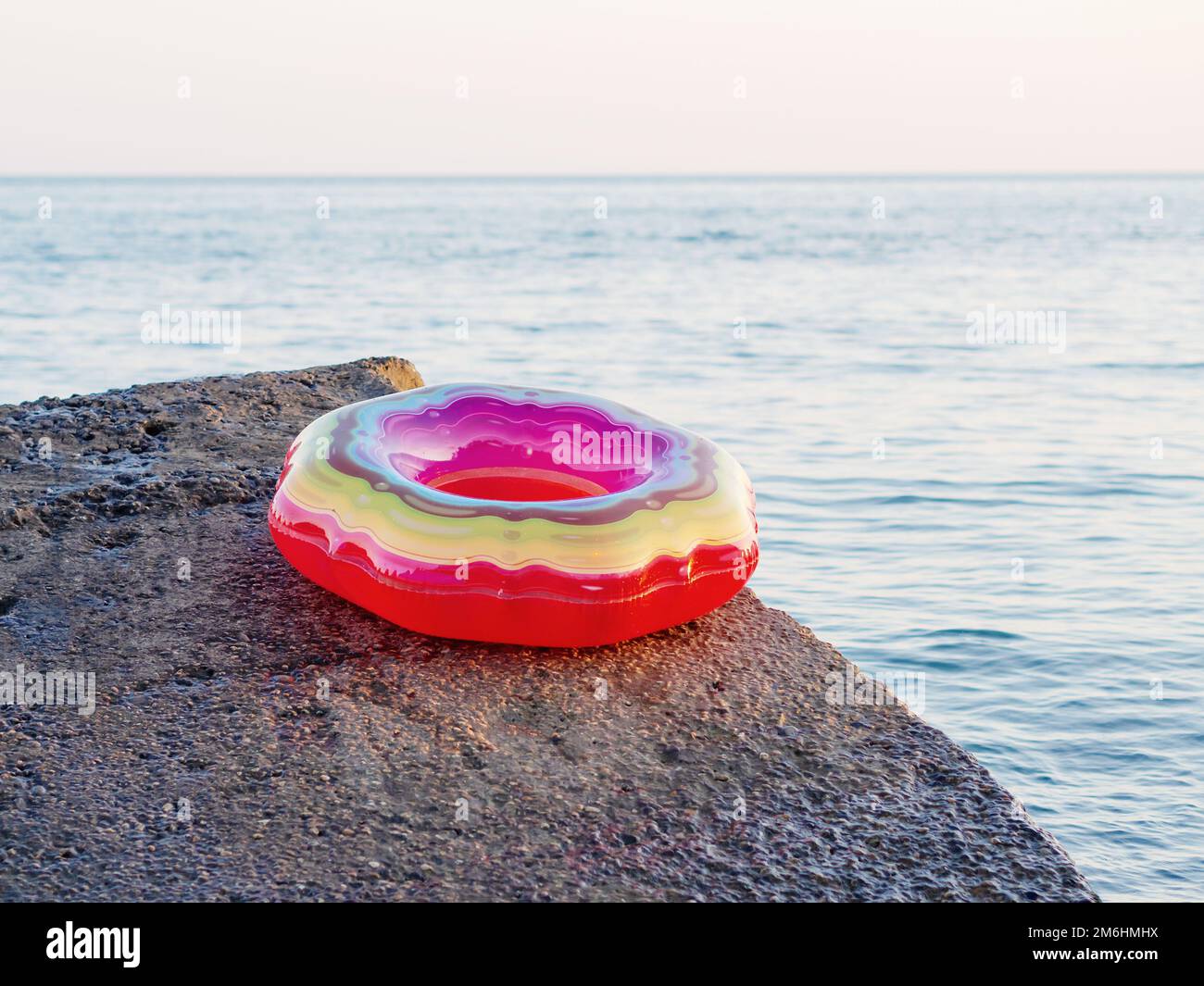 Un anneau de natation gonflable multicolore et lumineux se trouve au bord d'un brise-lames près de la mer Banque D'Images