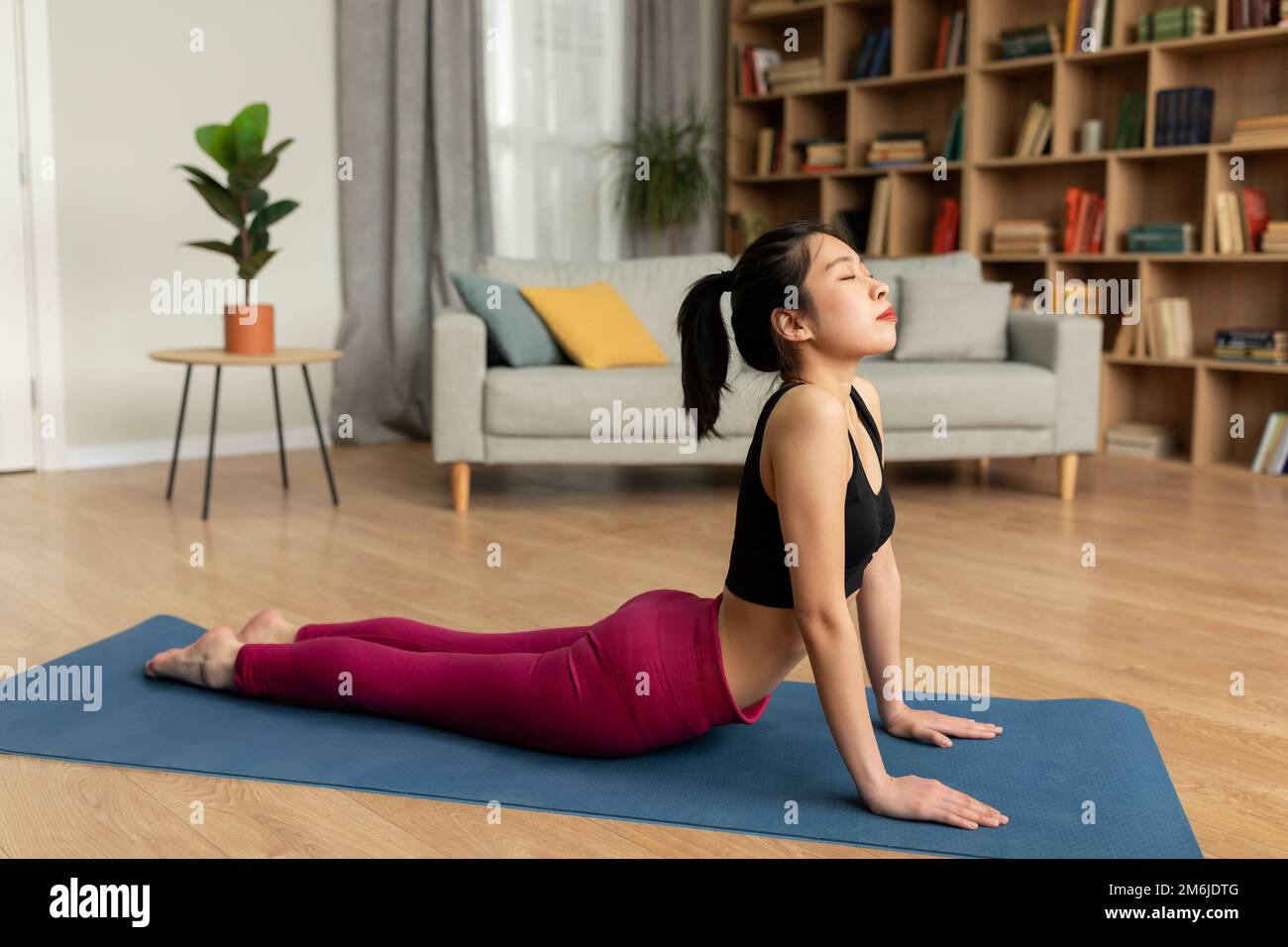 FIT femme coréenne faisant le yoga cobra pose ou pilates, s'entraîner sur le tapis dans le salon intérieur, espace de copie Banque D'Images