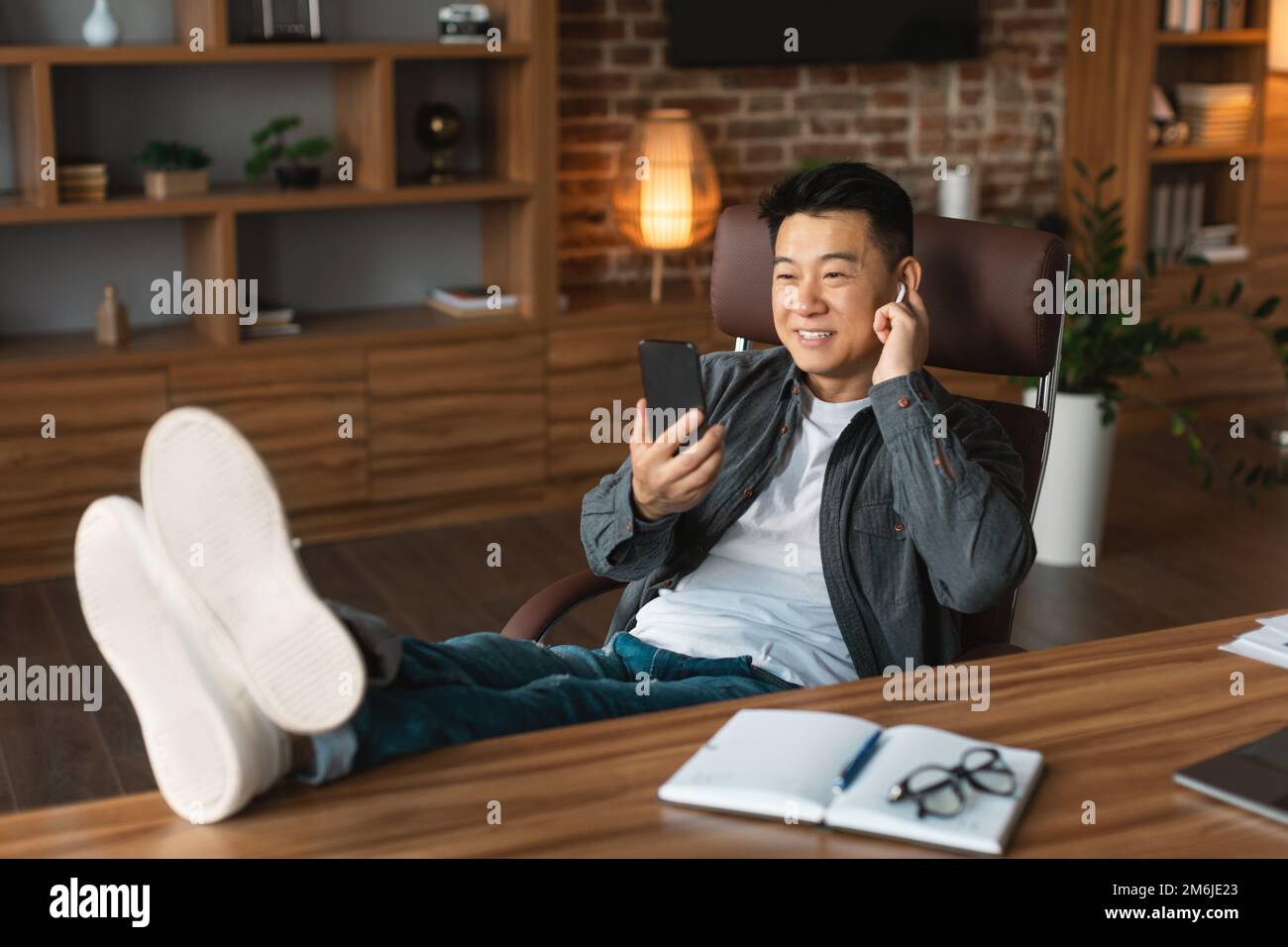 Je suis content que l'homme coréen adulte dans le casque sans fil ait des appels vidéo, regarde la webcam sur le lieu de travail avec un ordinateur portable Banque D'Images