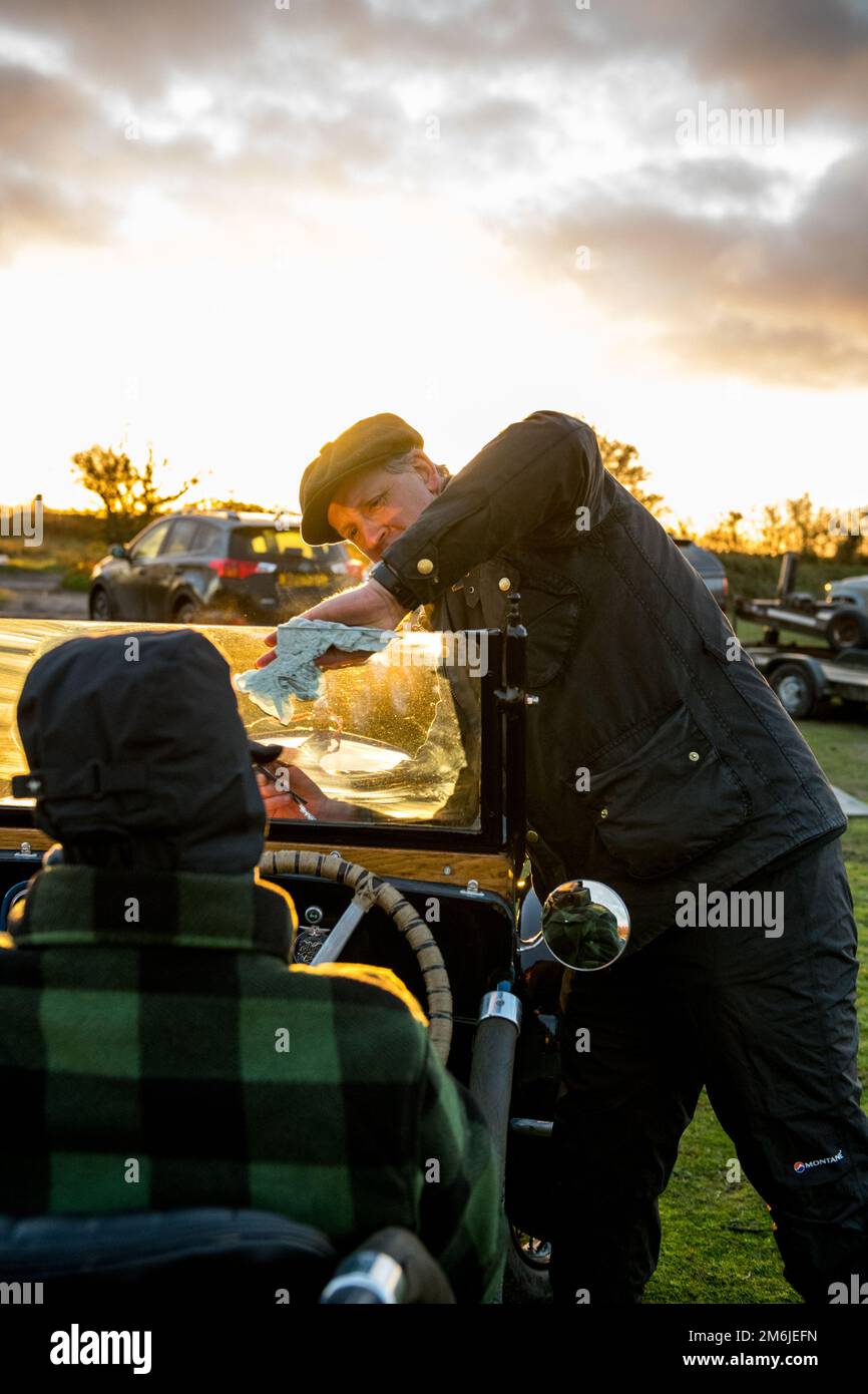 Un homme essuyant nettoyer le pare-vent avant d'une voiture d'avant guerre austin 7 à toit ouvert avec un chiffon propre avant les essais sur la colline du mémorial Dave Wilcox. Banque D'Images