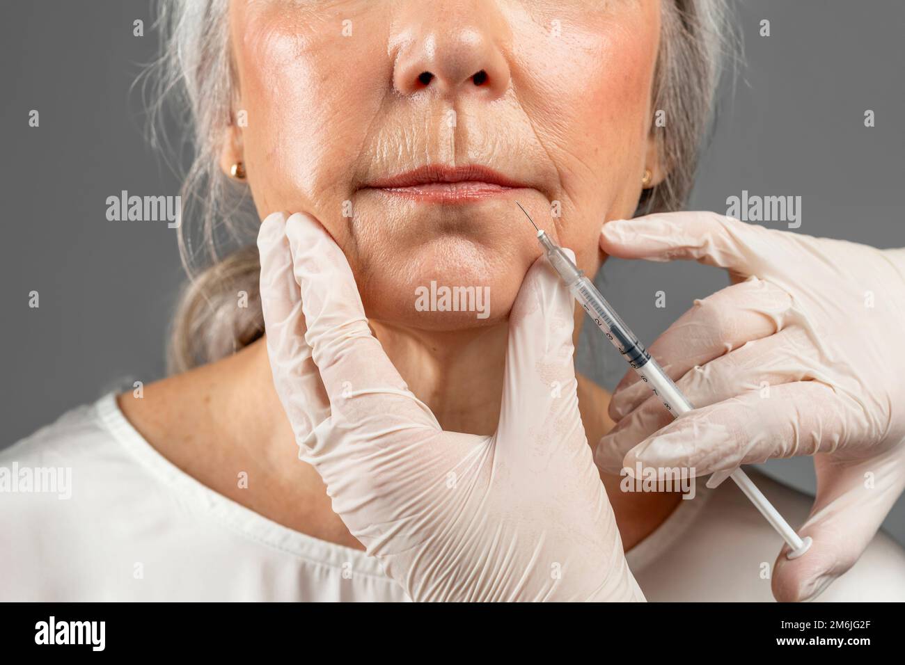 Femme européenne mûre sérieuse sur la procédure, les mains de cosmétologue en gants font l'injection de botox Banque D'Images