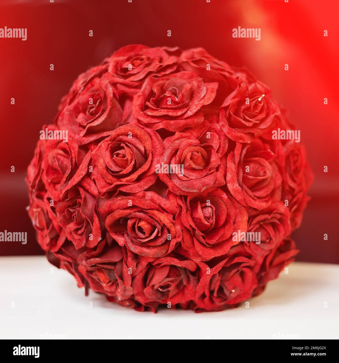 Une boule décorative de boutons roses rouges se dresse sur une surface blanche sur un fond rouge Banque D'Images