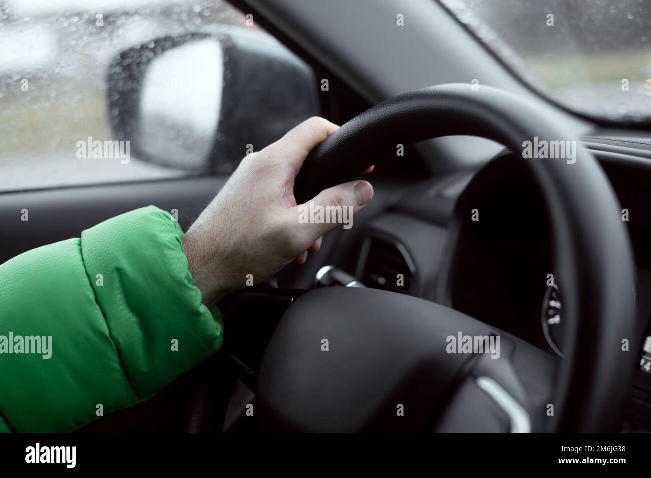 La main d'un homme tient le volant d'une voiture. Conduite d'une voiture par temps pluvieux. Mise au point douce. Banque D'Images