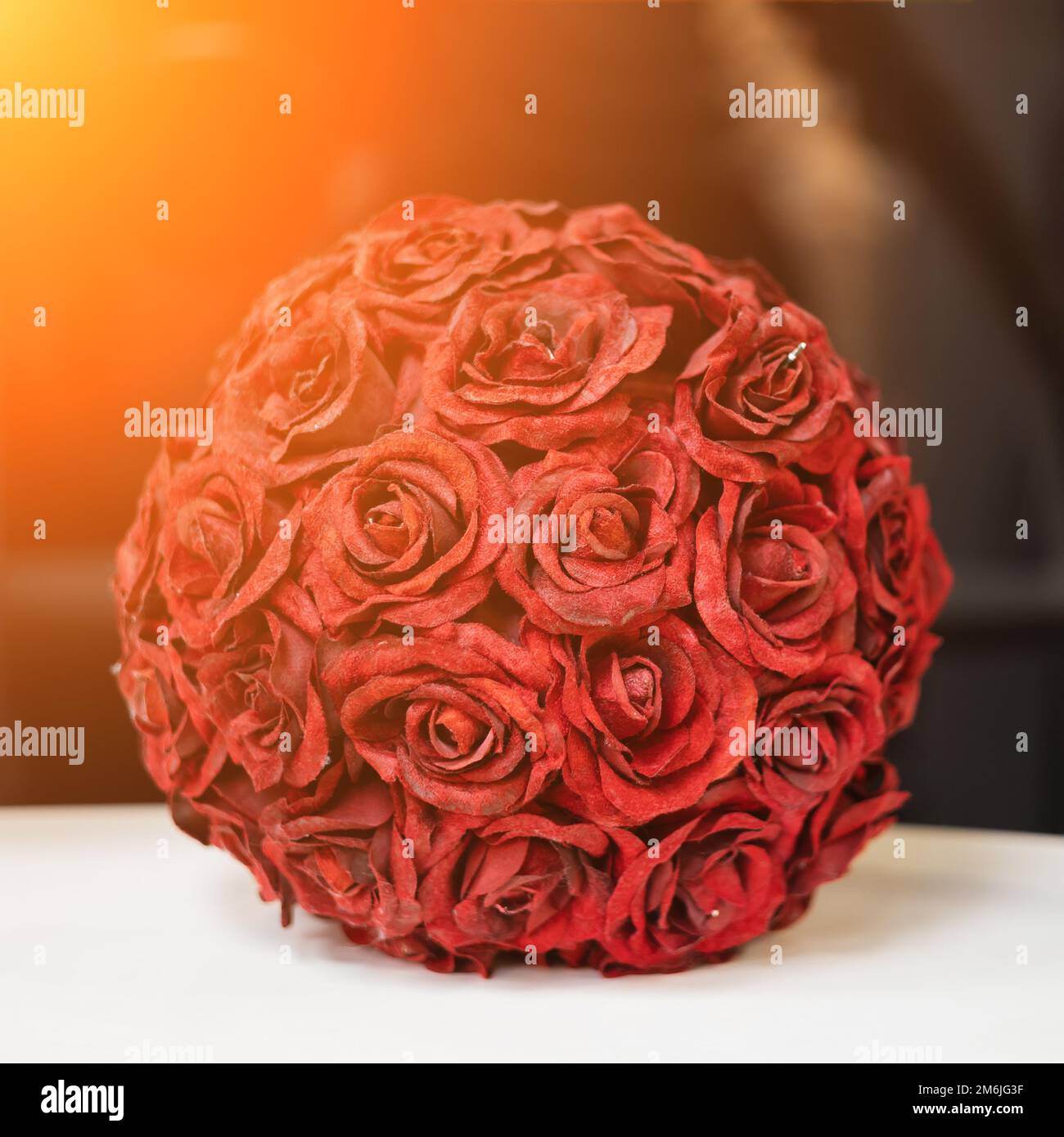 Une boule décorative de sépales roses rouges est placée sur une surface blanche à l'intérieur. Mise au point douce. Banque D'Images