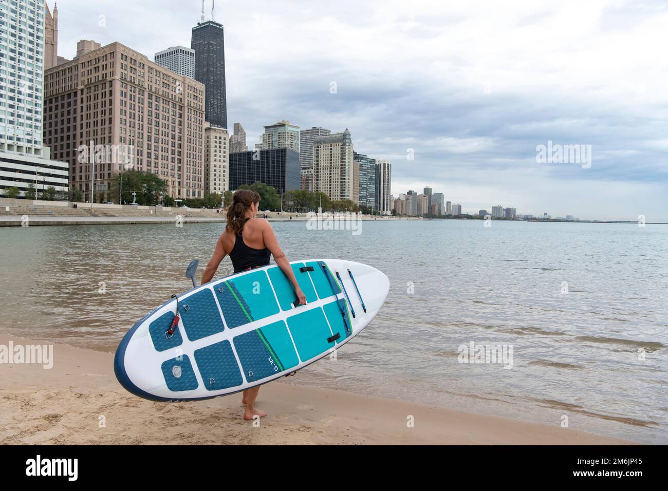femme transportant un paddleboard tout en marchant vers le lac dans la ville Banque D'Images