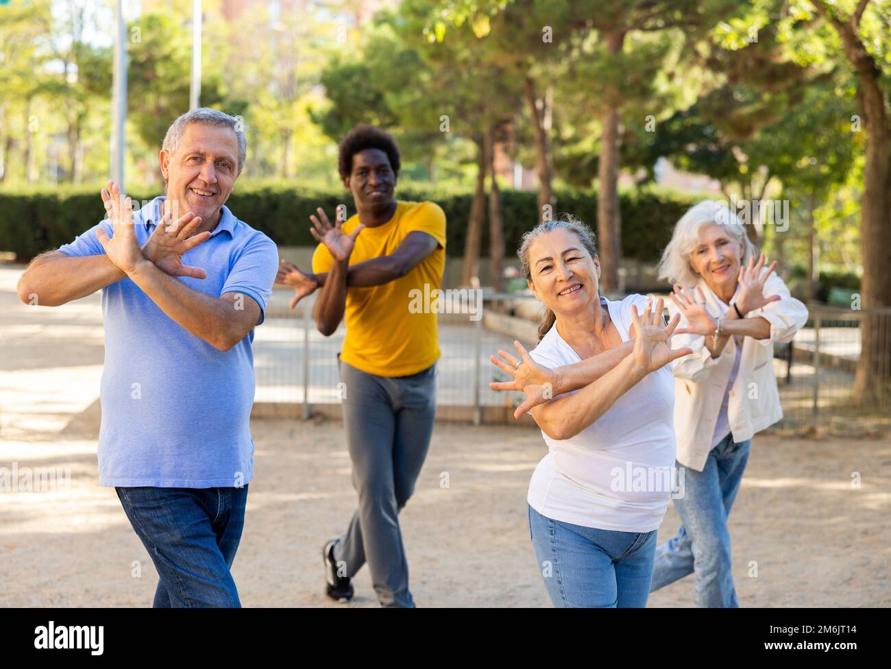 Un entraîneur afro-américain positif aidant les personnes âgées à étirer leurs muscles avant de danser à l'extérieur dans le parc Banque D'Images