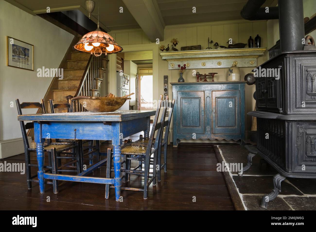Table à manger en bois peint en bleu antique et chaises avec four à bois en fonte noire dans la cuisine originale et salle à manger à l'intérieur de la vieille maison de 1785. Banque D'Images