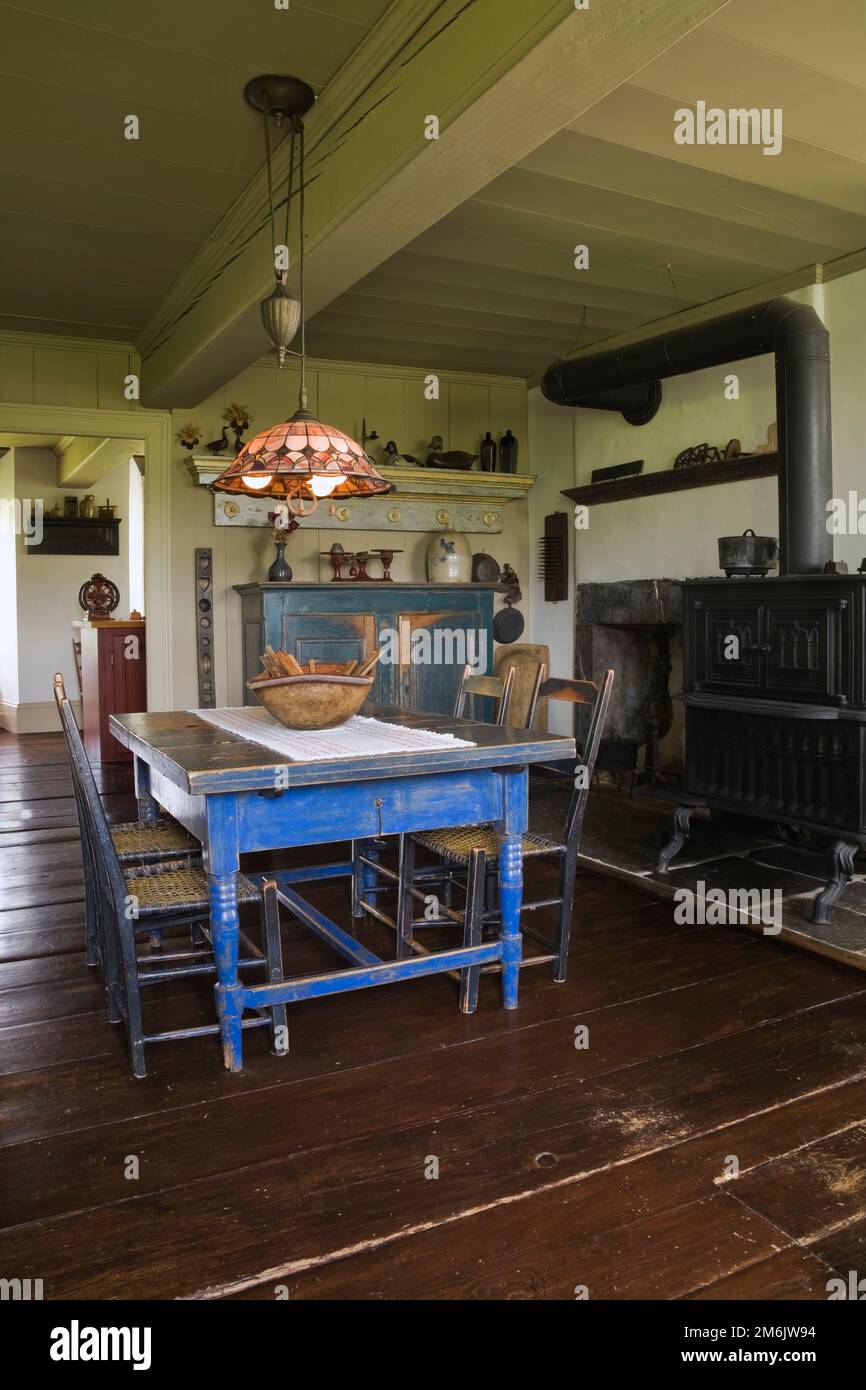 Table à manger en bois peint en bleu antique et chaises avec four à bois en fonte noire dans la cuisine originale et salle à manger à l'intérieur de la vieille maison de 1785. Banque D'Images