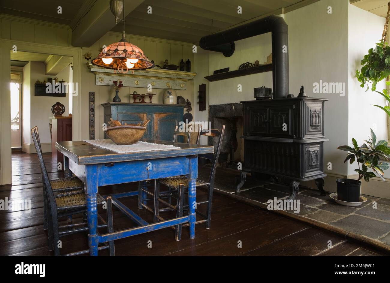 Table à manger en bois peint en bleu antique et chaises avec four à bois en fonte noire dans la cuisine originale et salle à manger à l'intérieur de la vieille maison de 1785. Banque D'Images