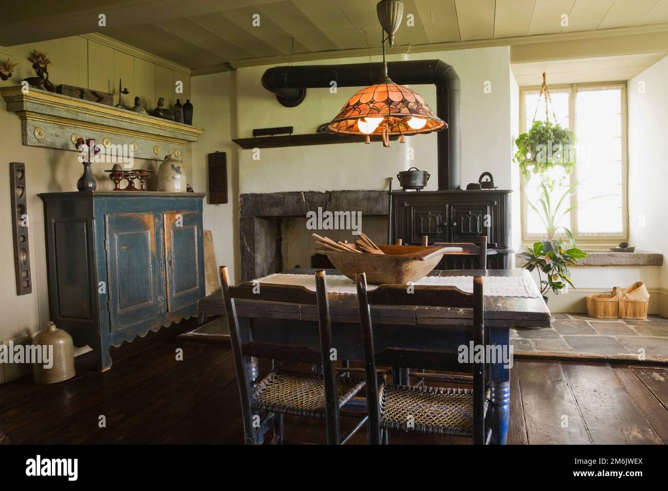 Table à manger en bois peint en bleu antique et chaises avec four à bois en fonte noire dans la cuisine originale et salle à manger à l'intérieur de la vieille maison de 1785. Banque D'Images