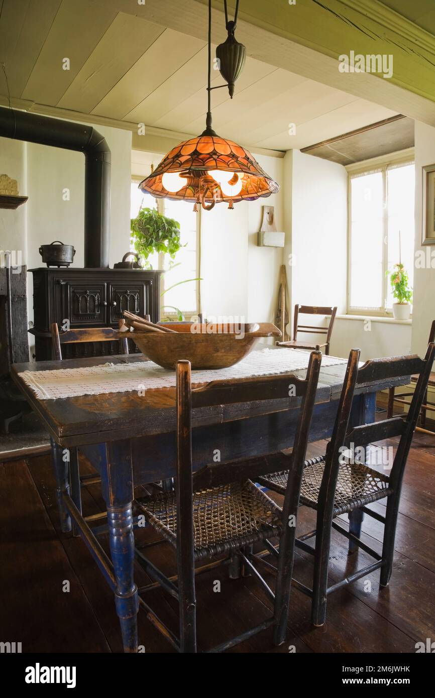 Table à manger en bois peint en bleu antique et chaises avec four à bois en fonte noire dans la cuisine originale et salle à manger à l'intérieur de la vieille maison de 1785. Banque D'Images