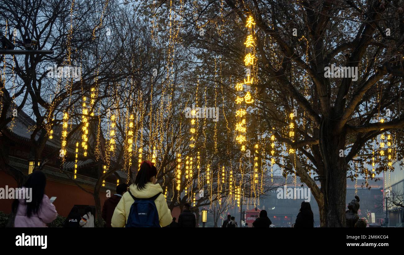 XI'AN, CHINE - 4 JANVIER 2023 - des copybooks lumineux sont vus sur les arbres tandis que les touristes se promèdent le long d'une rue piétonne à la grande Pagode Wild Goose pittoresque sp Banque D'Images