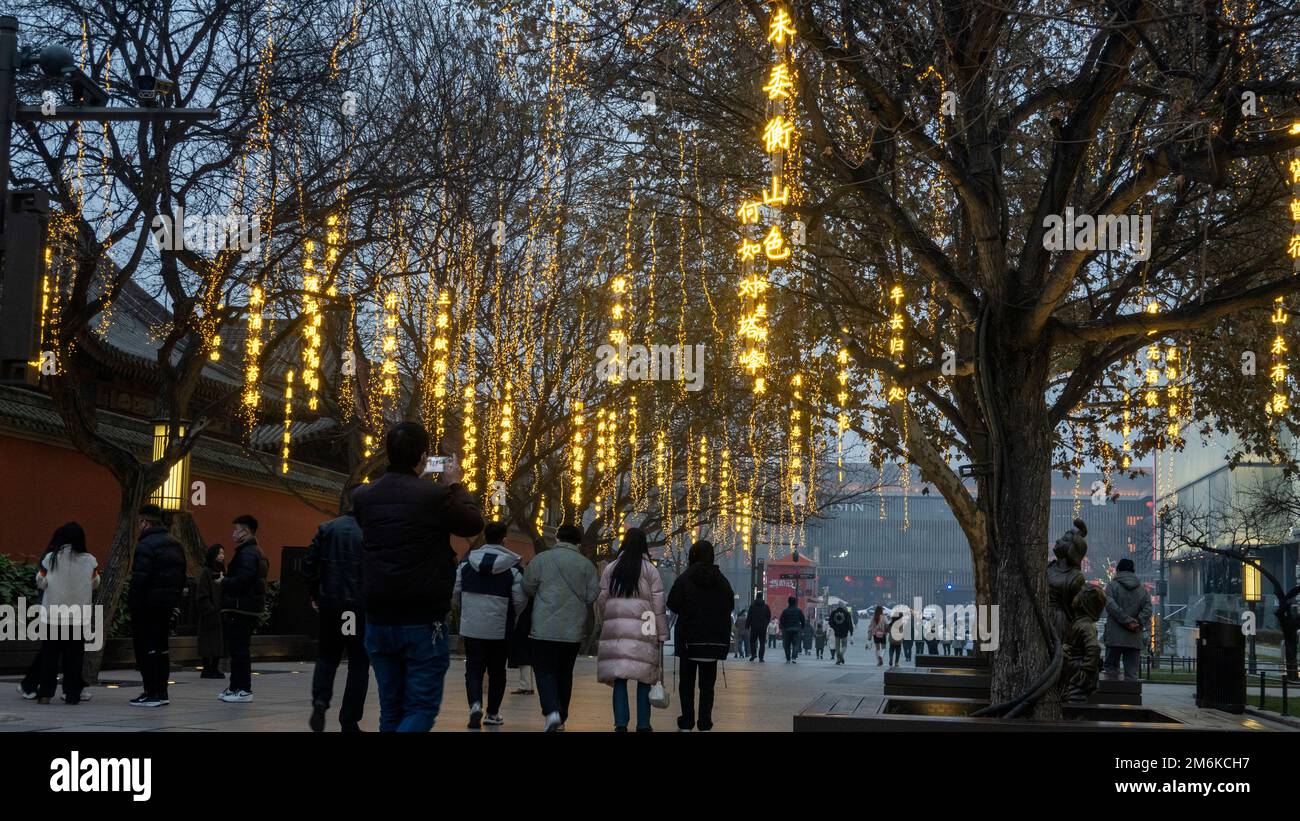 XI'AN, CHINE - 4 JANVIER 2023 - des copybooks lumineux sont vus sur les arbres tandis que les touristes se promèdent le long d'une rue piétonne à la grande Pagode Wild Goose pittoresque sp Banque D'Images