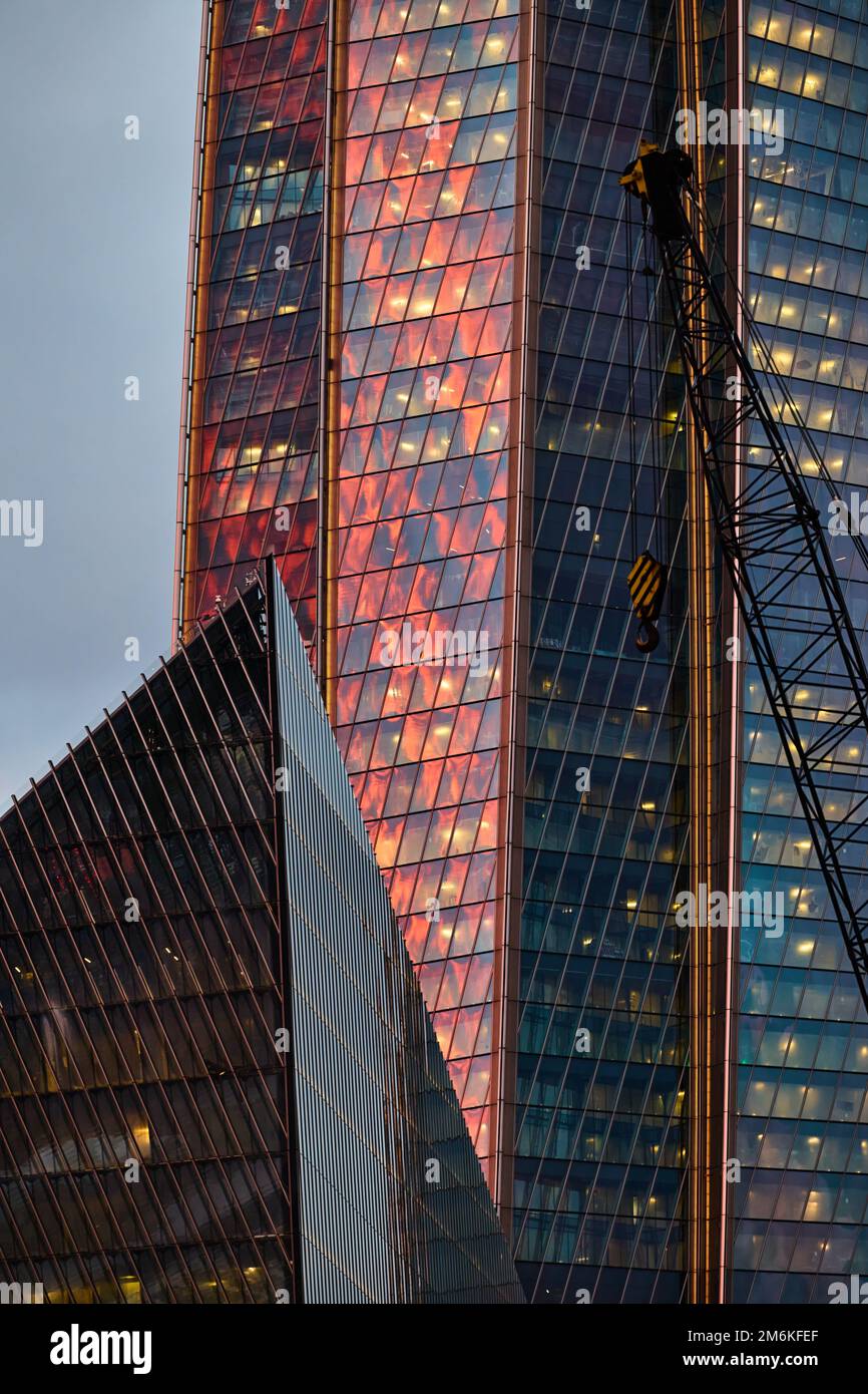 La façade en verre et en fer d'un énorme gratte-ciel au coucher du soleil, acier, couleur orange, reflet du soleil Banque D'Images