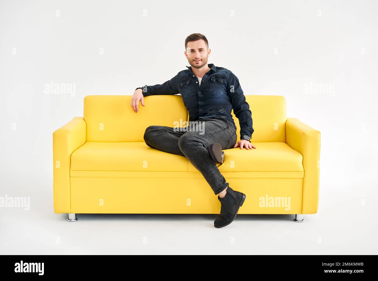 Jeune homme branché posant assis sur un canapé jaune regardant un appareil photo Banque D'Images