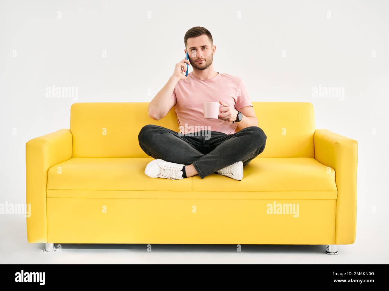 Homme détendu parlant sur le téléphone portable et de boire du café assis sur le confortable canapé lumineux Banque D'Images