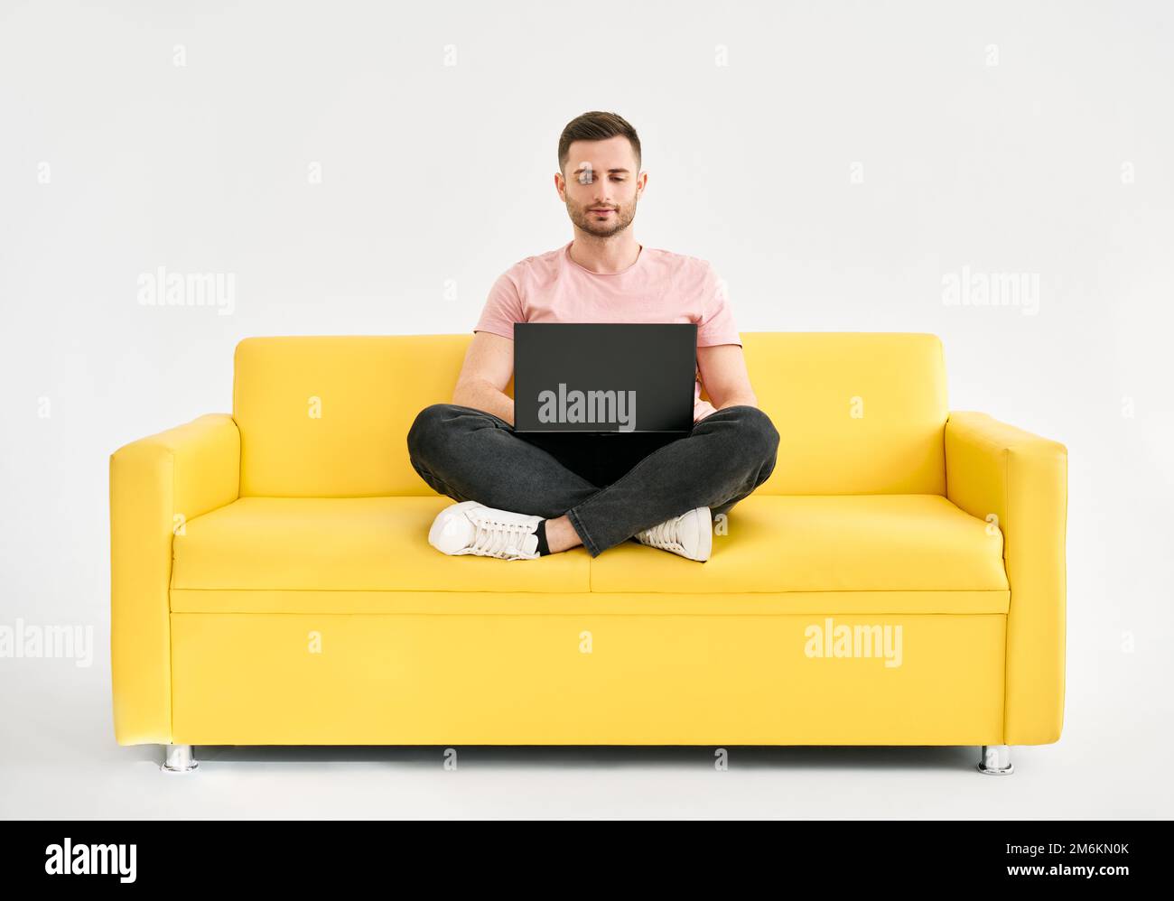 Homme détendu utilisant un ordinateur portable assis sur un canapé jaune sur fond blanc Banque D'Images