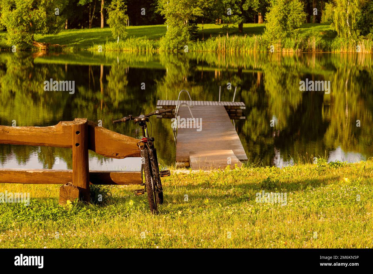 Vélo de sport moderne appuyé contre un banc en bois au bord du lac Banque D'Images