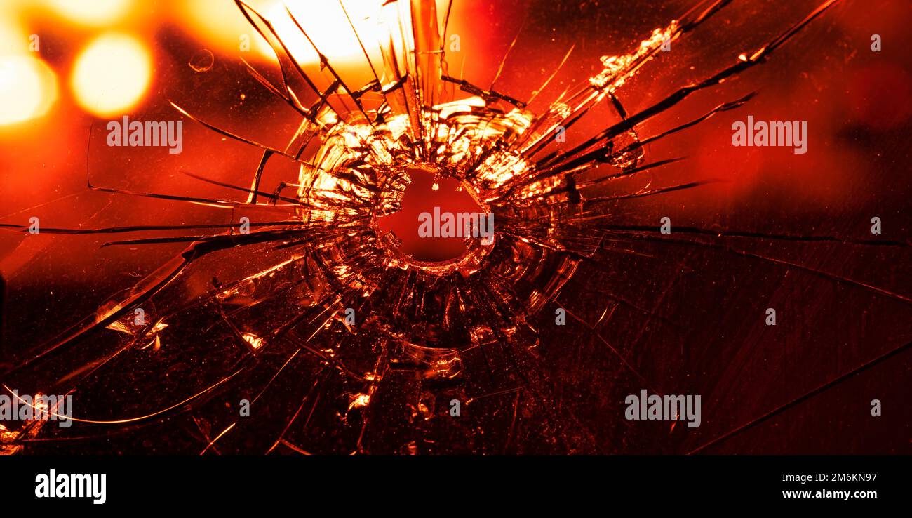 Fissures dans le verre, un trou de balle, sur un fond de flammes focalisées. Arrière-plan ou texture abstrait. Banque D'Images