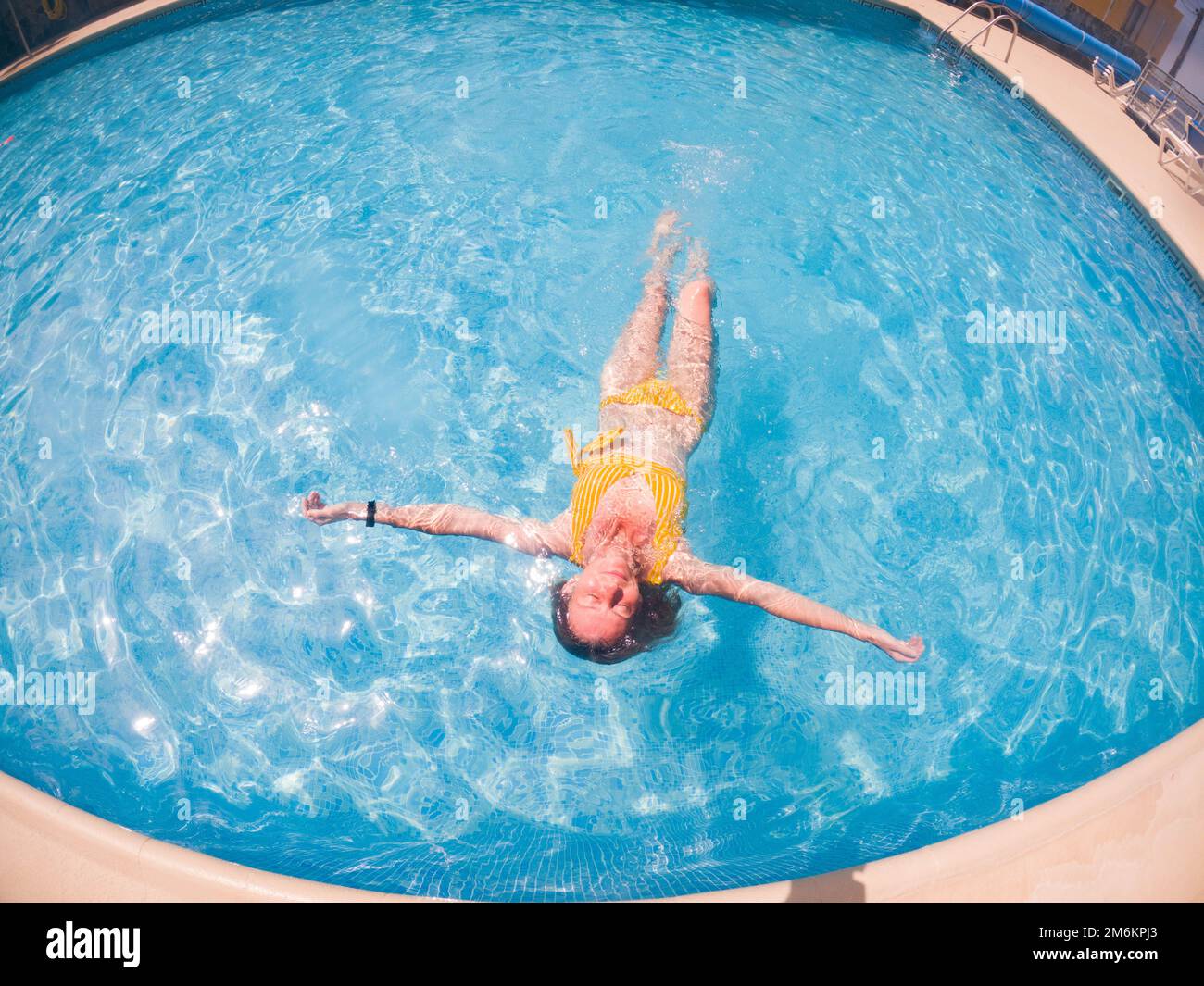 Femme en maillot de bain jaune dans de l'eau bleu clair dans la piscine Banque D'Images