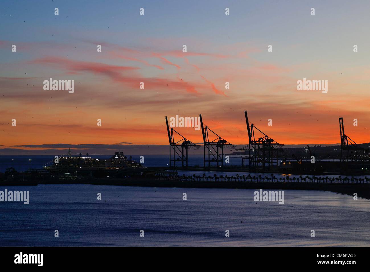 Vue sur le coucher du soleil avec silhouette de grues industrielles dans le port de Malaga, Andalousie, Espagne. Banque D'Images