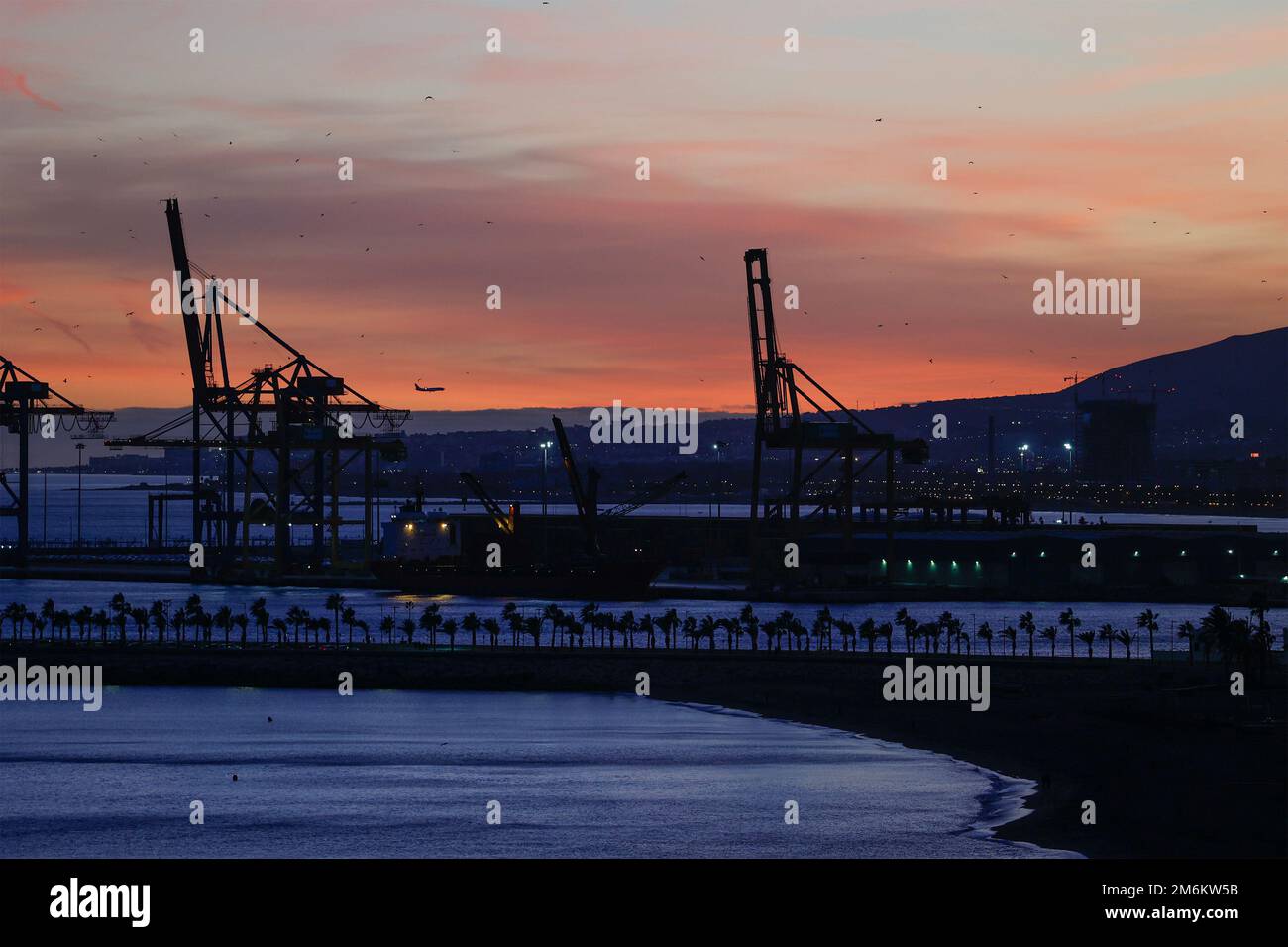 Vue sur le coucher du soleil avec silhouette de grues industrielles dans le port de Malaga, Andalousie, Espagne. Banque D'Images