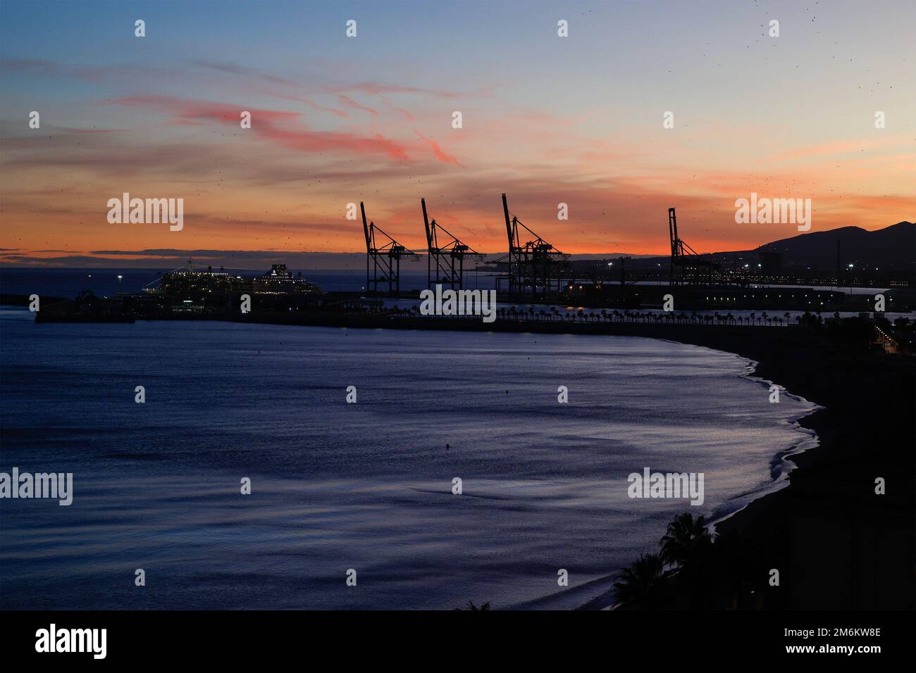 Vue sur le coucher du soleil avec silhouette de grues industrielles dans le port de Malaga, Andalousie, Espagne. Banque D'Images