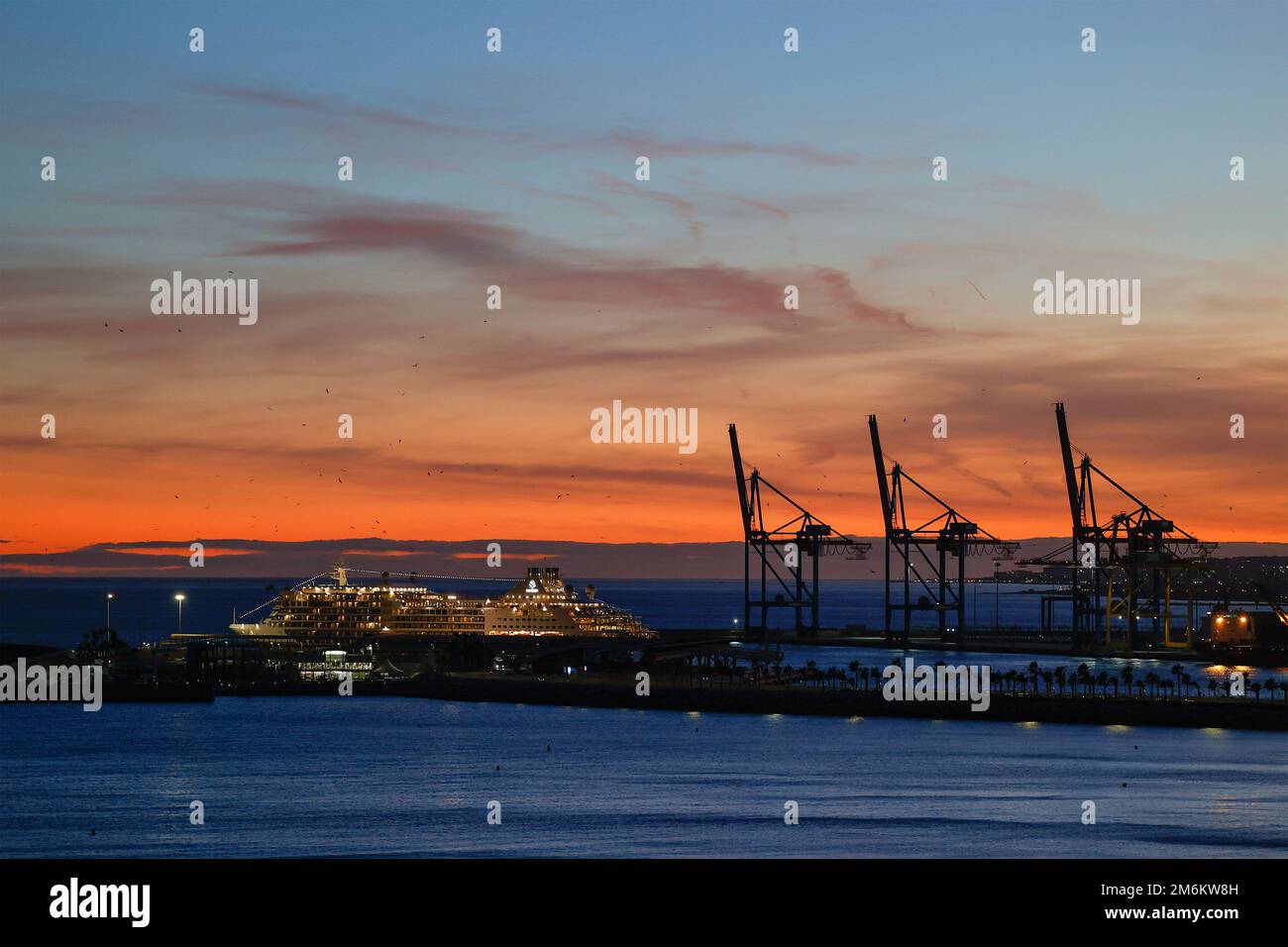 Vue sur le coucher du soleil avec silhouette de grues industrielles dans le port de Malaga, Andalousie, Espagne. Banque D'Images