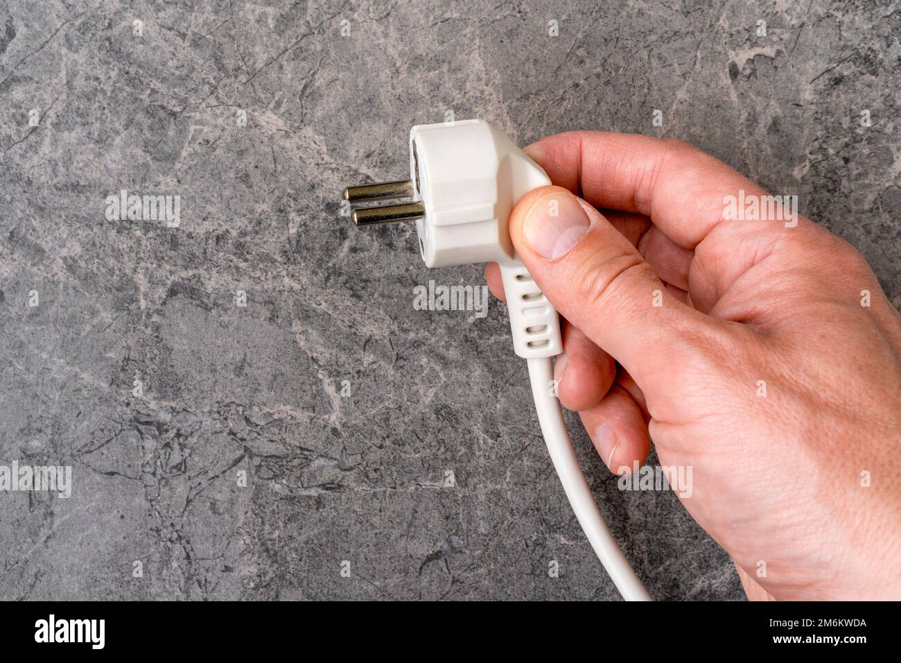 Main avec une fiche d'alimentation blanche sur fond de pierre Banque D'Images