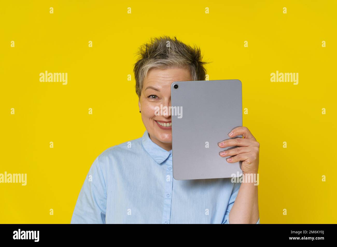 Femme mûre aux cheveux gris avec une peau derrière un Tablet pc travaillant en ligne ou sur les réseaux sociaux. Jolie femme en 50s portant un chemisier bleu isol Banque D'Images