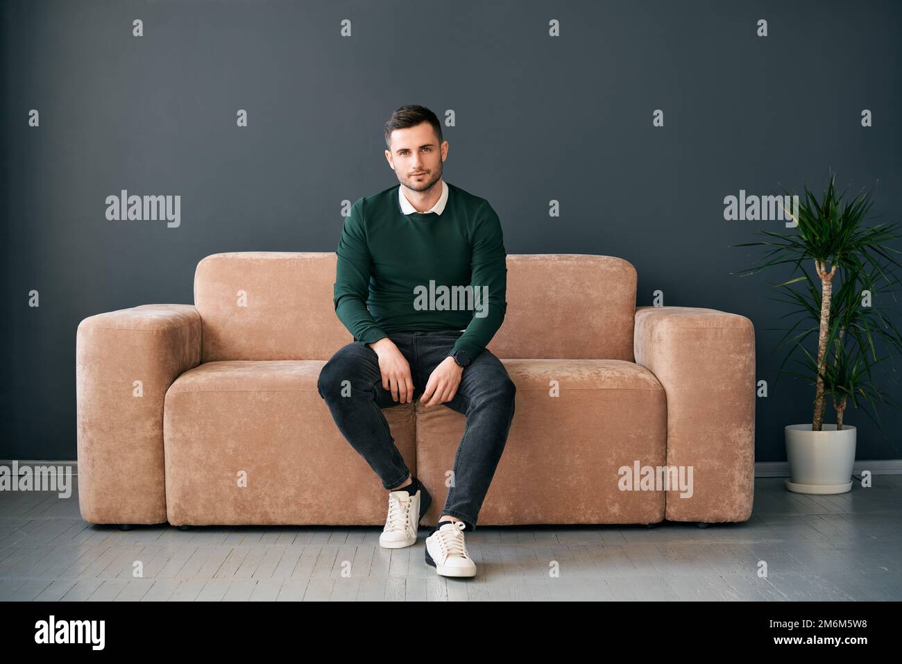 Jeune homme tendance se posant assis sur un canapé et regardant un appareil photo Banque D'Images