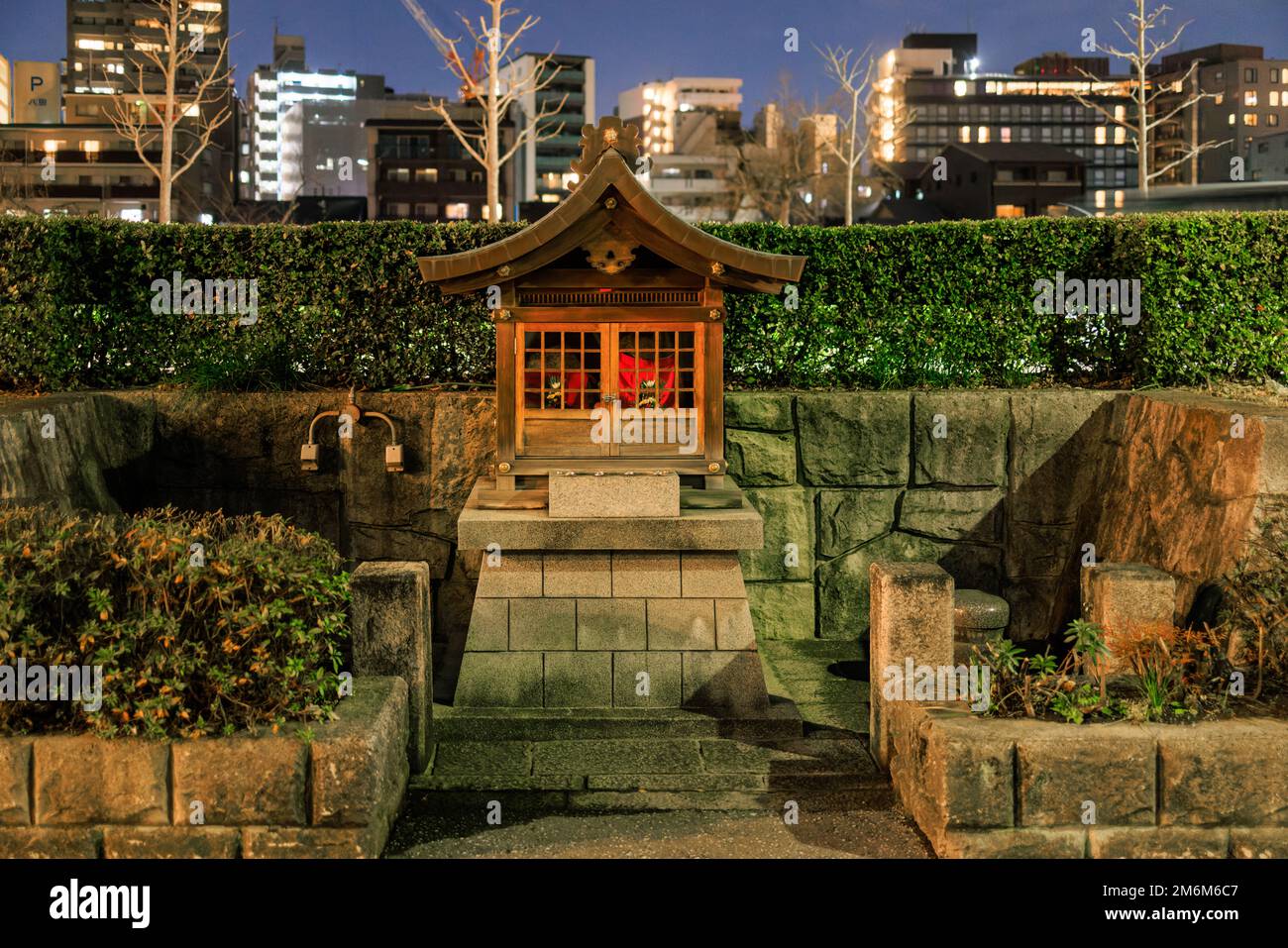 Petit sanctuaire en bois sur une plate-forme en pierre dans la ville japonaise la nuit Banque D'Images