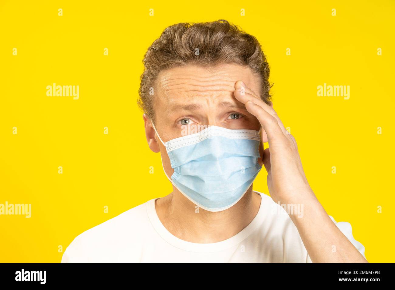 Le jeune homme souffrant d'un mal de tête tient sa tête portant un masque médical sur son visage. Un jeune homme malade se sent sous le masque mig Banque D'Images