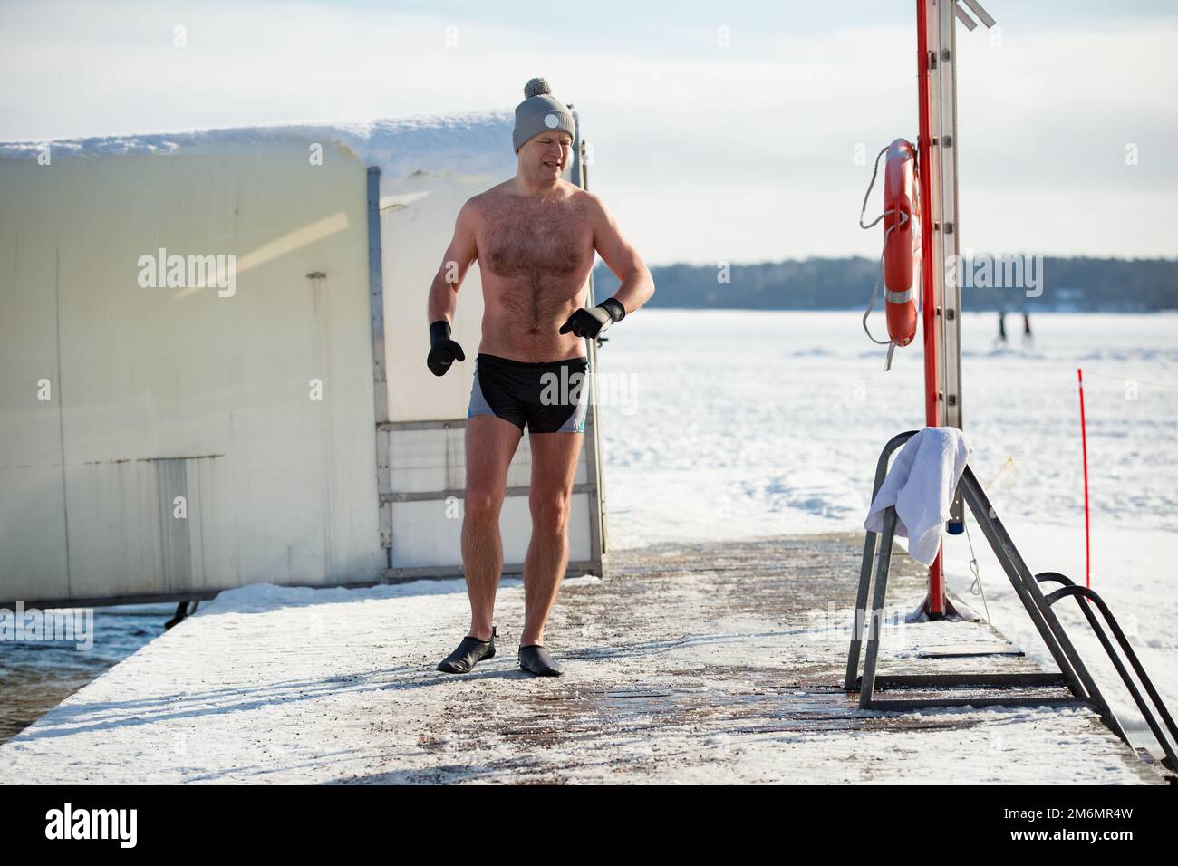 Un homme dans un chapeau chaud et des gants nageant dans un trou de glace, marchant le long de la jetée. En hiver, en Finlande. Un mode de vie sain Banque D'Images
