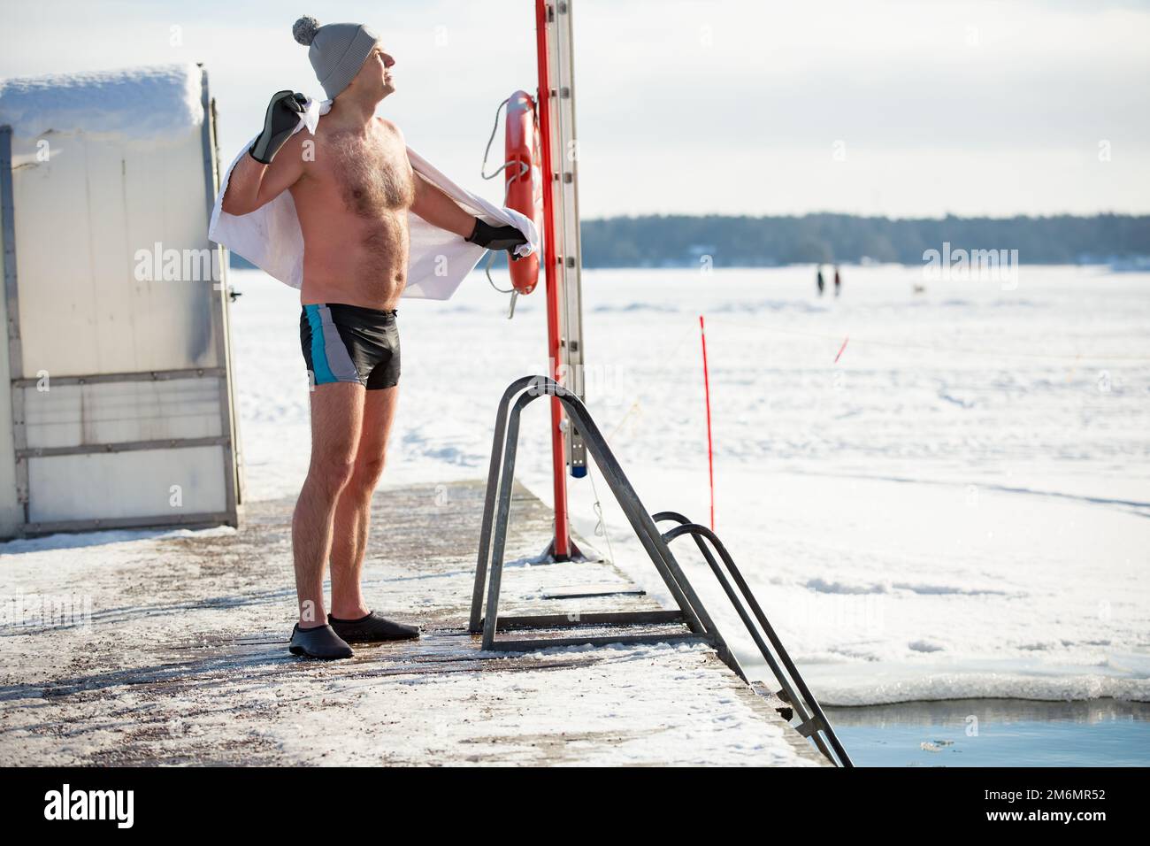 Un homme dans un chapeau chaud et des gants nageant dans un trou de glace, séchant avec une serviette. En hiver, en Finlande. Un mode de vie sain Banque D'Images