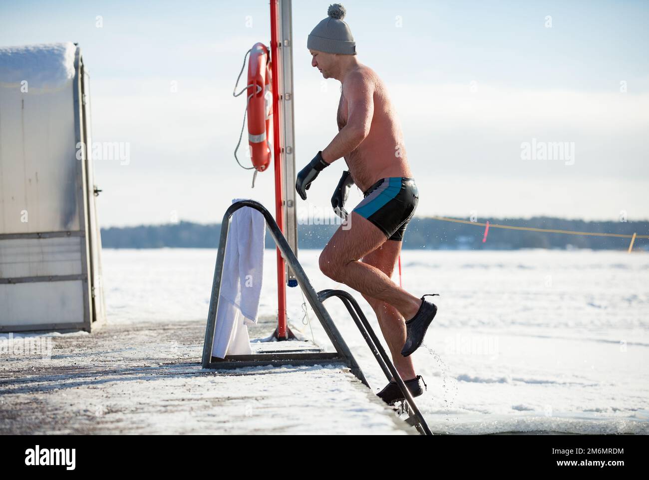 Un homme dans un chapeau chaud et des gants nageant dans un trou de glace, sortant de l'eau. En hiver, en Finlande. Un mode de vie sain Banque D'Images