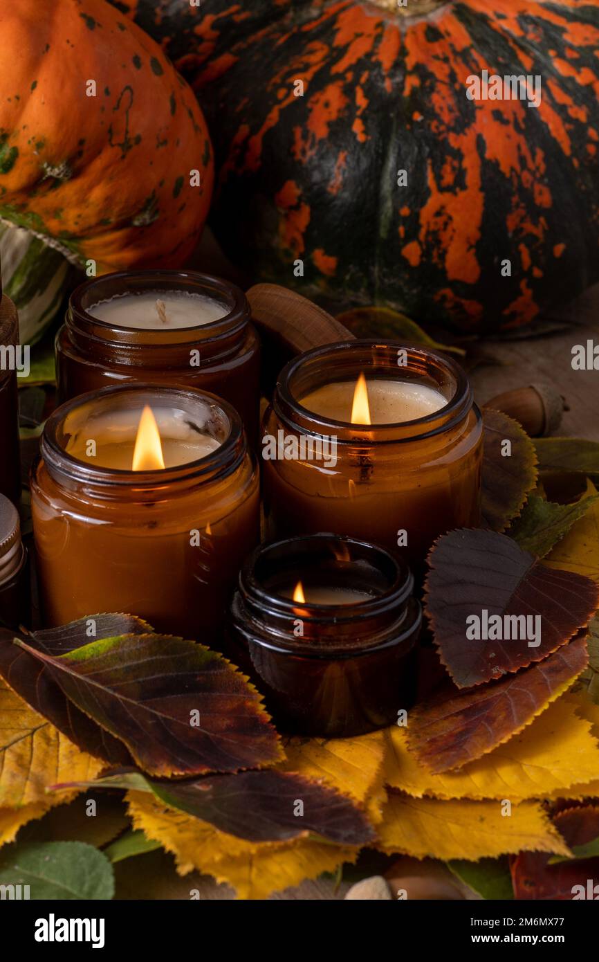 Les bougies de soja brûlent dans des pots en verre. Feuilles d'arbre, citrouille. Confort à la maison. Bougie dans un pot brun. Parfum et lumière. Bougie parfumée faite à la main. Aromathérapie. Ambiance d'automne. Décoration chaleureuse à l'automne. Banque D'Images
