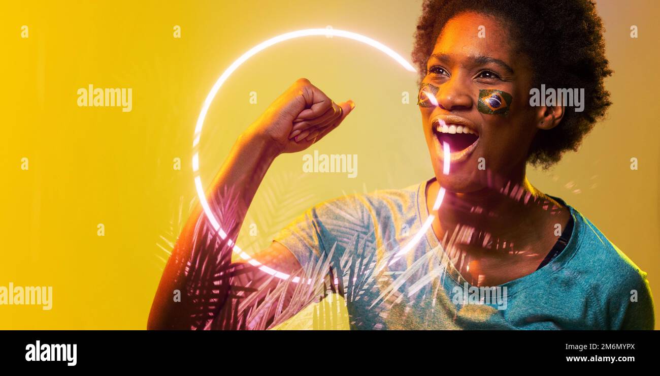 Fan afro-américain avec le visage du drapeau brésilien peint criant par le cercle et les plantes Banque D'Images