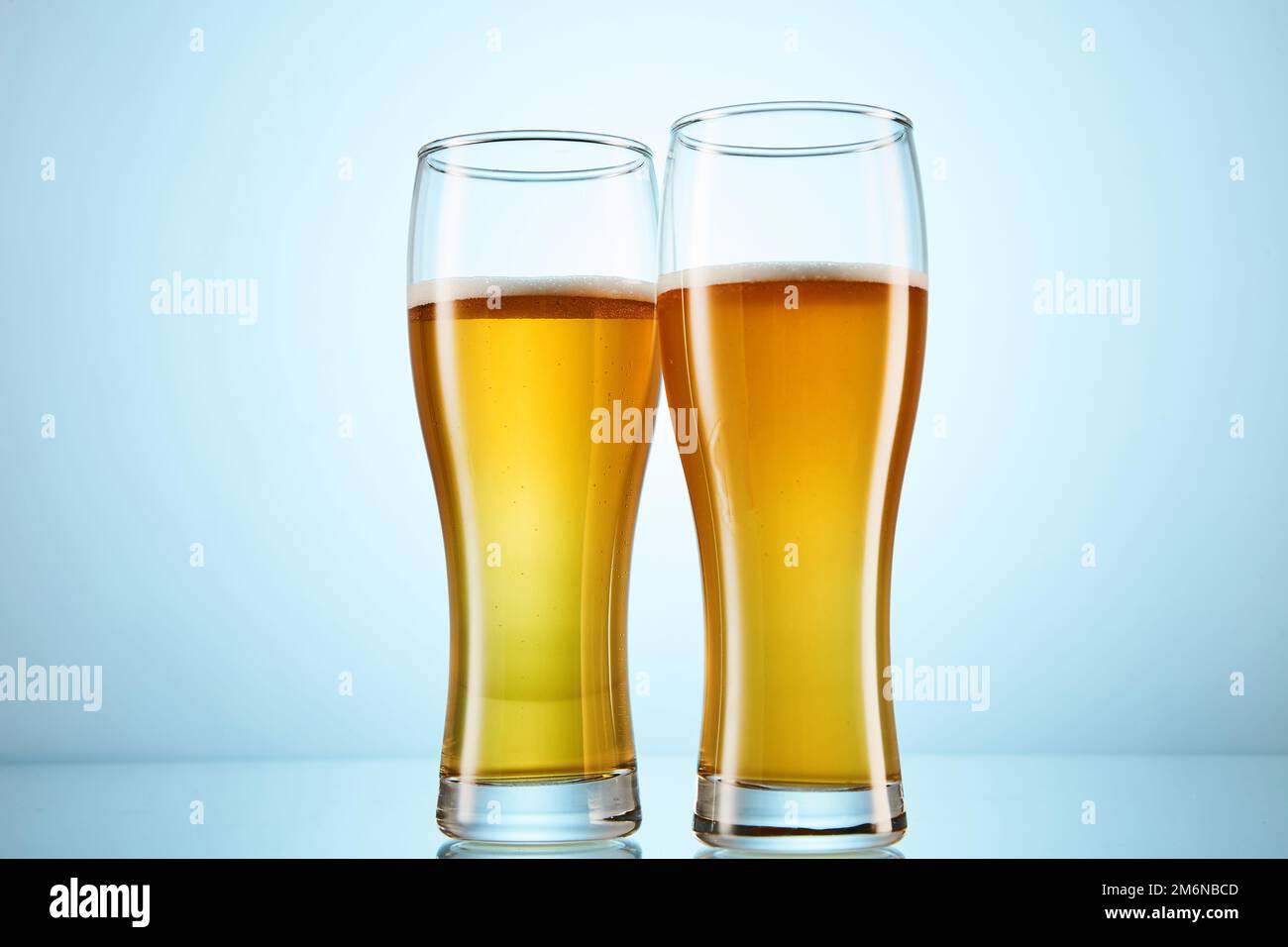 Bière jaune gazeuse versée dans de grands verres sur bleu clair. Banque D'Images