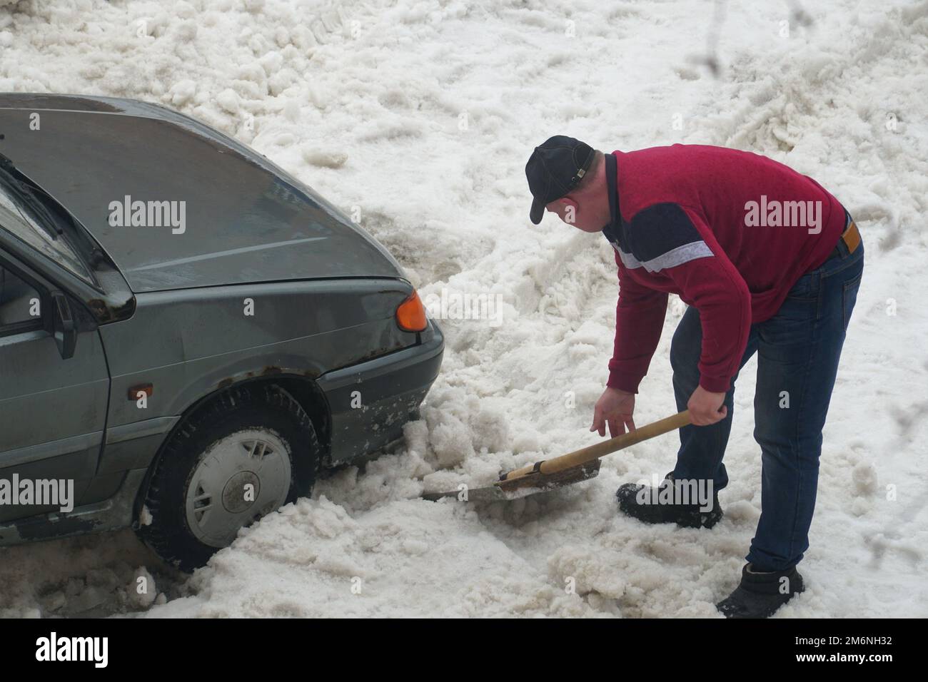 Un homme creuse une pelle de neige d'une voiture coincée dans la neige Banque D'Images