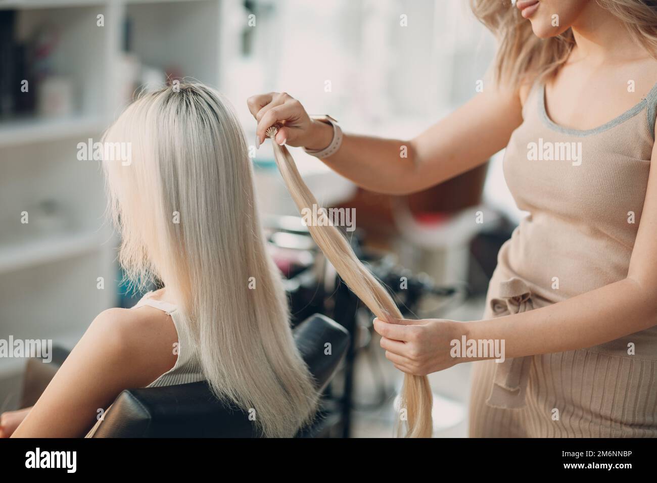 Coiffeur femme faisant des extensions de cheveux à la jeune femme avec des cheveux blonds dans le salon de beauté. Rallonge de cheveux professionnelle. Banque D'Images