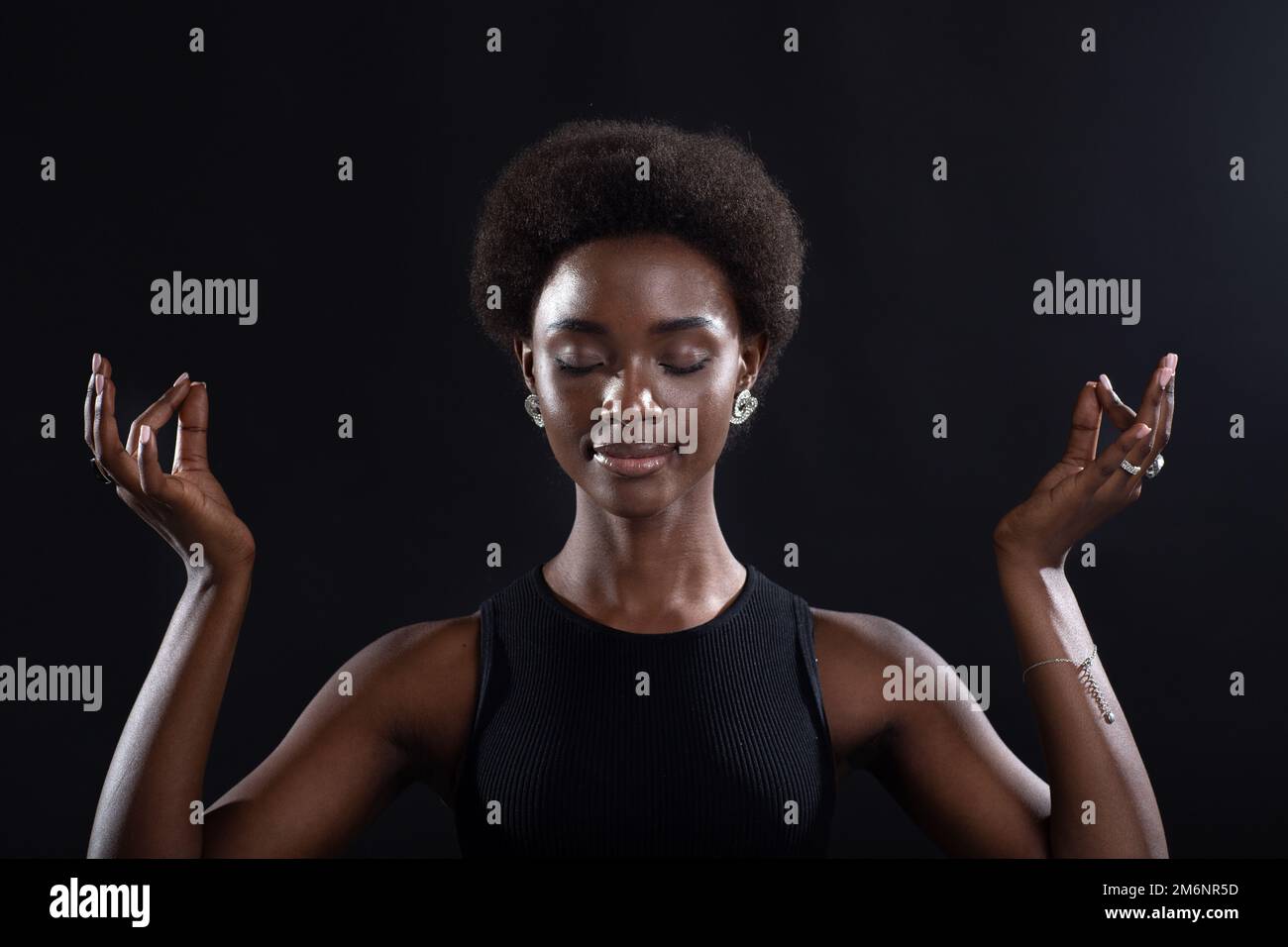 Portrait de studio de la femme afro-américaine montrant un geste zen ou OK.Femme méditant sur fond noir. Banque D'Images