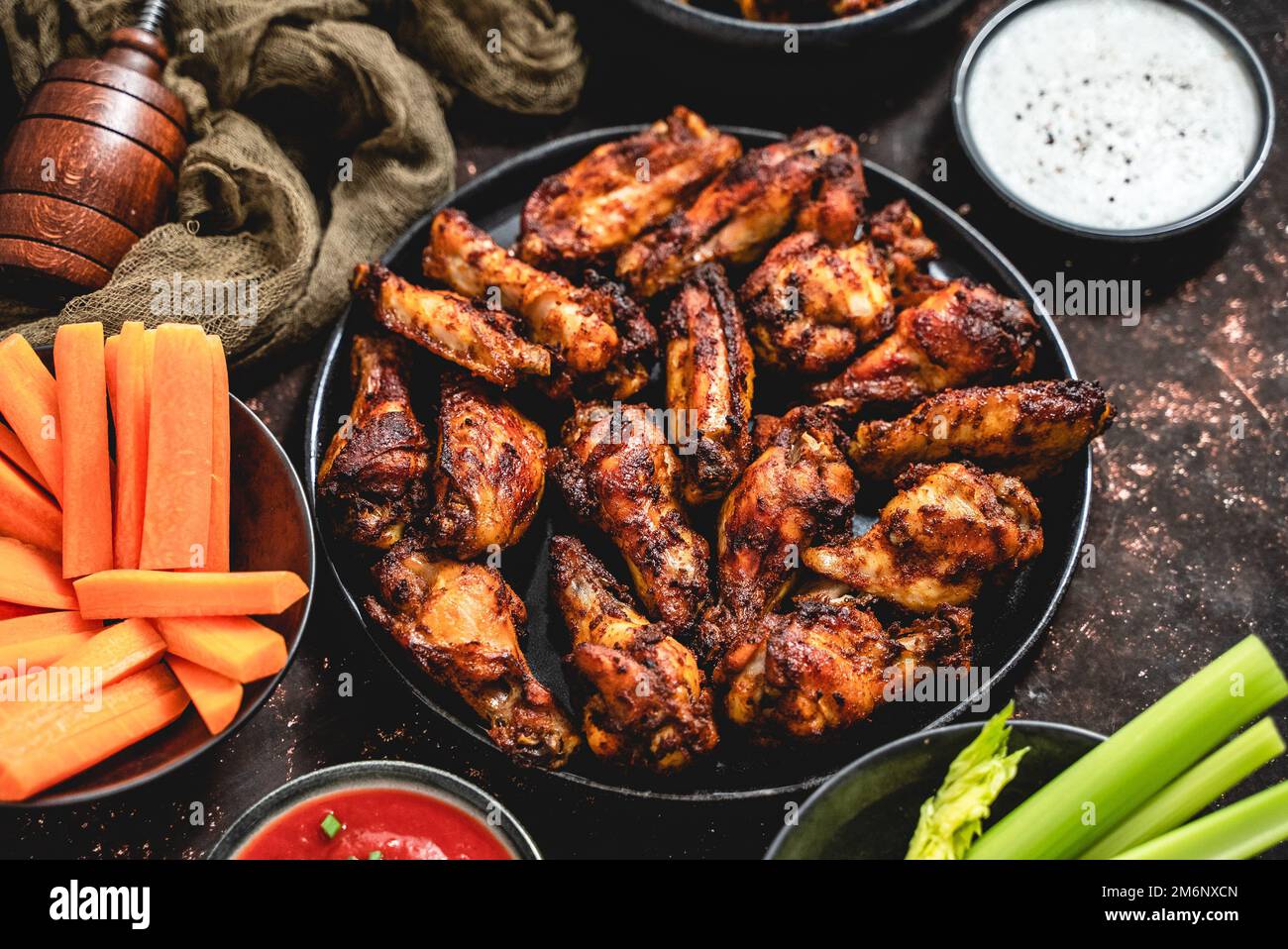 Ailes de poulet grillées sur une assiette noire sur un fond rustique foncé Banque D'Images