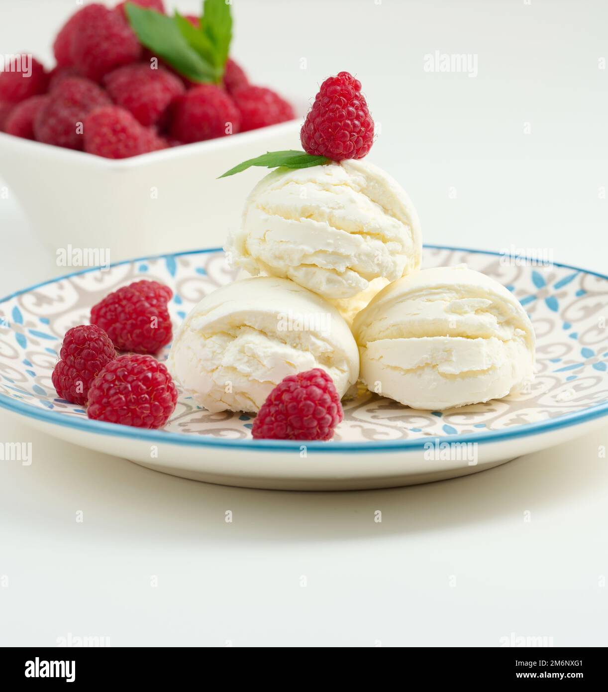 Boules de glace à la vanille aux framboises rouges dans une assiette ronde Banque D'Images
