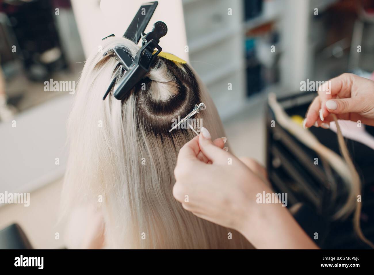 Coiffeur femme faisant des extensions de cheveux à la jeune femme avec des cheveux blonds dans le salon de beauté. Rallonge de cheveux professionnelle. Banque D'Images