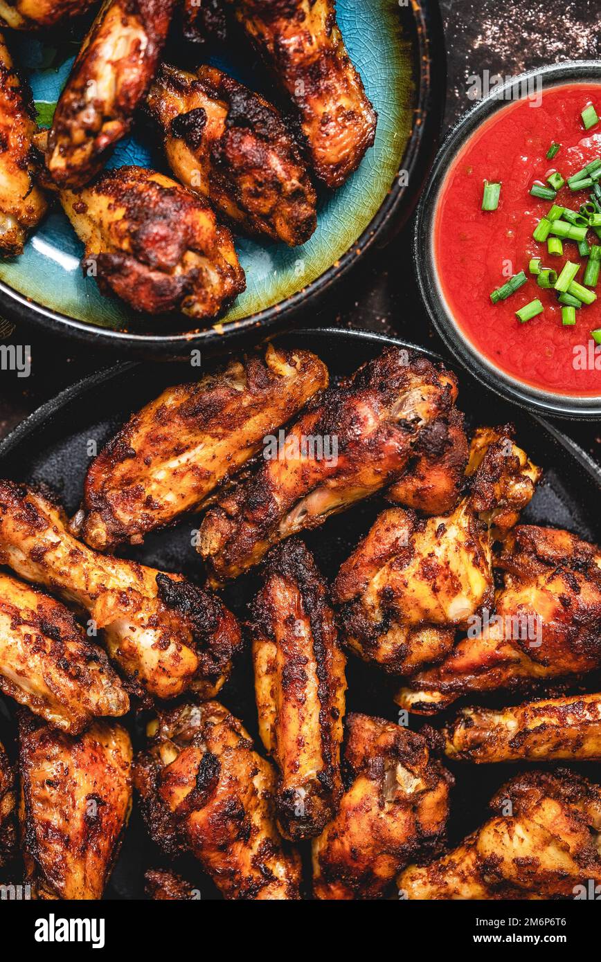 Ailes de poulet grillées sur une assiette noire sur un fond rustique foncé Banque D'Images