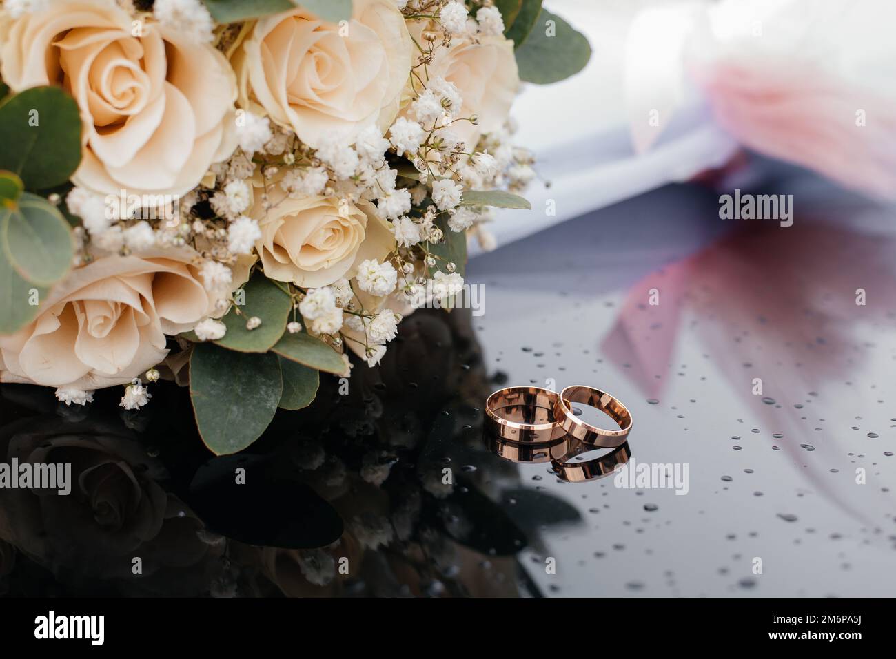 Une belle image aux tons avec des anneaux de mariage se trouve sur une surface noire sur le fond d'un bouquet de fleurs Banque D'Images Une belle image aux tons avec des anneaux de mariage se trouve sur une surface noire sur le fond d'un bouquet de fleurs Banque D'Images